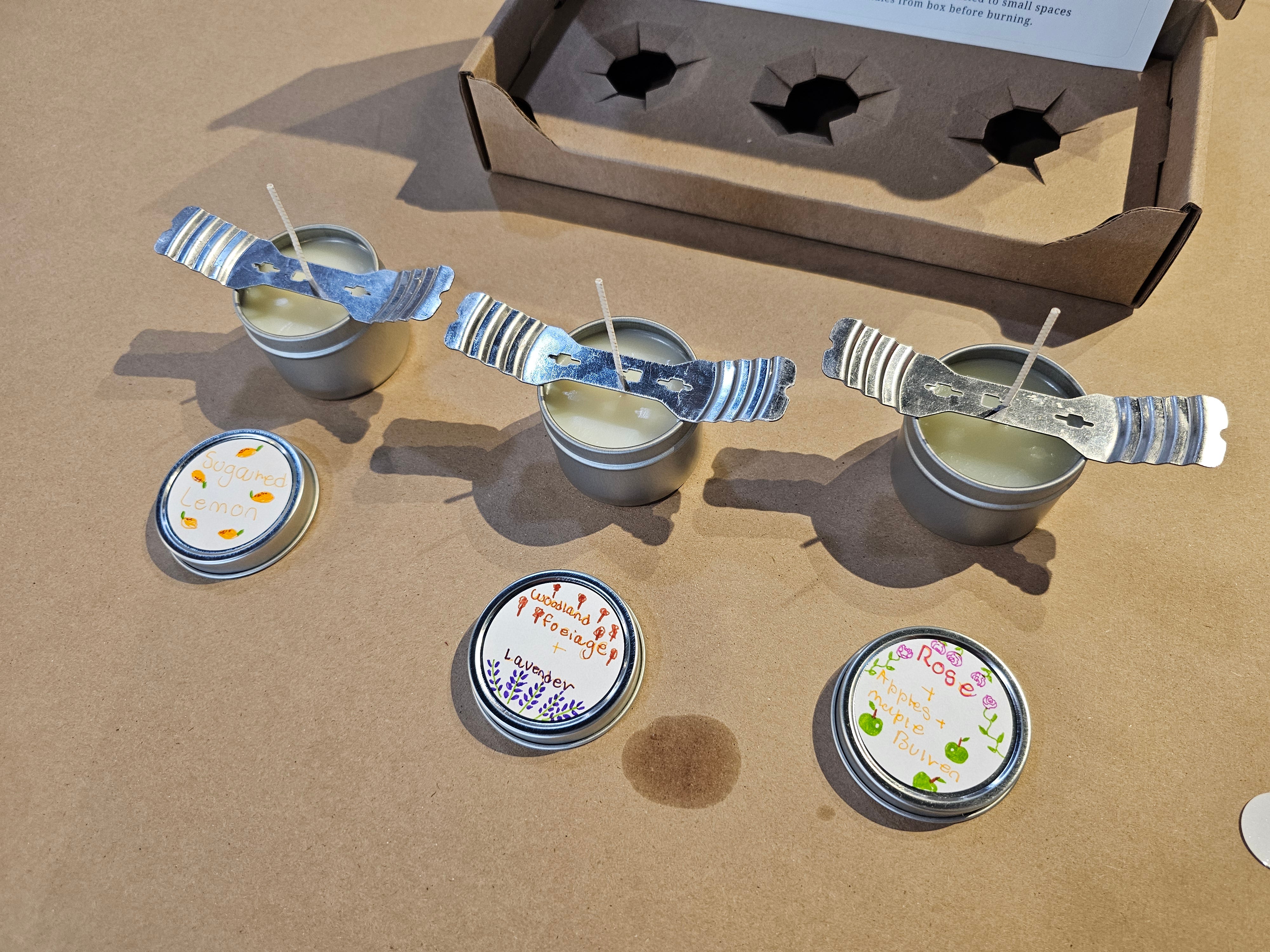 Small candles with lids on a brown surface, with a cardboard box in the background.